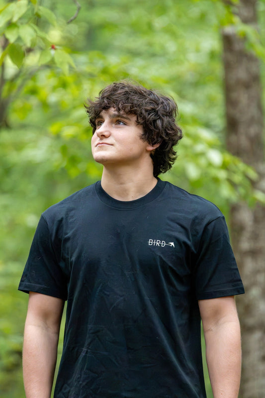 Green Narrows Illustrated tee — back view, worn in the woods