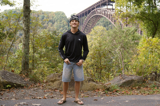 Man wearing the black BIRD Explorer sun hoodie below the New River Gorge Bridge