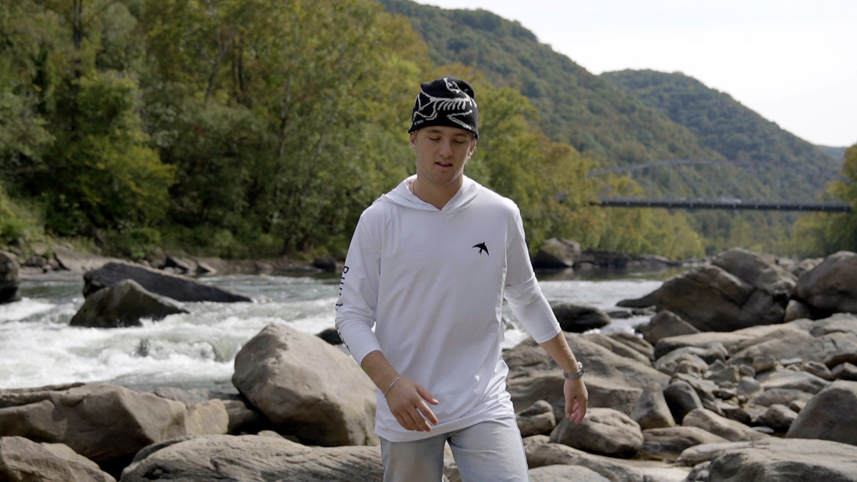 Man wearing the white BIRD Explorer sun hoodie beside rapids on the New River